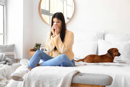 A woman sneezing on a bed next to a dog.