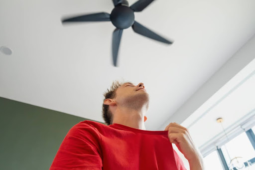 A man standing under a ceiling fan in a home.