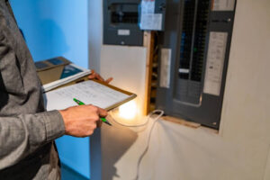 A man holding a clipboard and inspecting an electrical panel in a home.