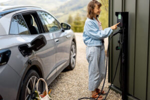 A woman charging an electric vehicle with an EV charging station that has been installed in the driveway.